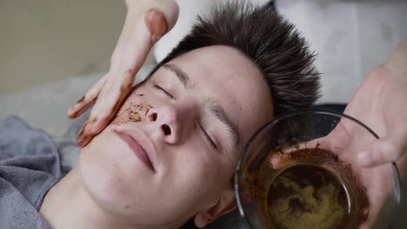Beautician's Hand Applies Coffee Scrub on Man's Face Skin with Massage Movements