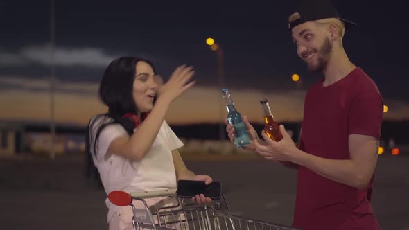 Middle Shot of Joyful Young Woman Standing on Empty Parking Lot with Trolley at Night As Cheerful