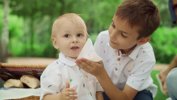 Brother Taking Care About Small Boy at Picnic. Mother Hand Giving Cherry To Boy