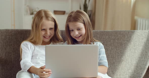 Direct View of Two Little Smiling Sisters Looking at Laptop. Portrait of Girls Children Use Computer