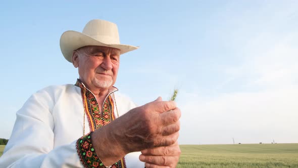 An Old Grandfather in an Embroidered Shirt Against a Sky Holds an Ear of Wheat and Shows a Thumb