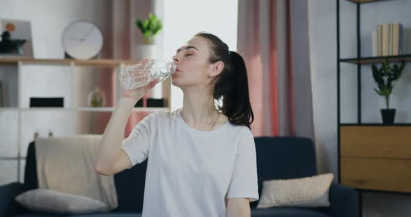 Young Brunette in white t-shirt which Drinking Water After Home Workout