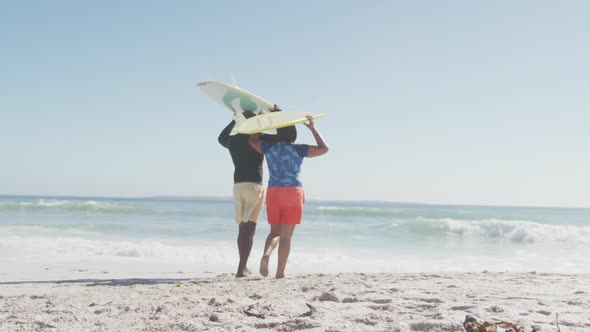 Senior african american couple walking with surfboards on sunny beach