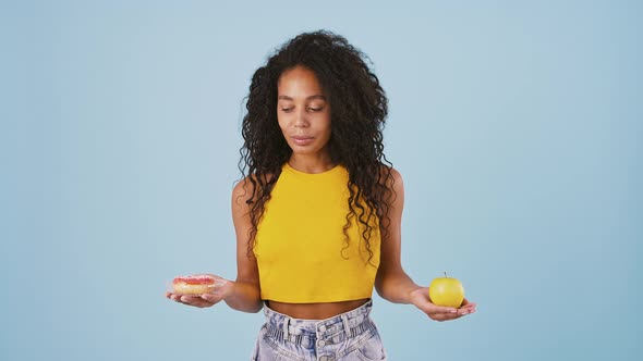 Afroamerican Model Taking Out Apple and Donut From Behind Her Back Thinking What Should She Eat