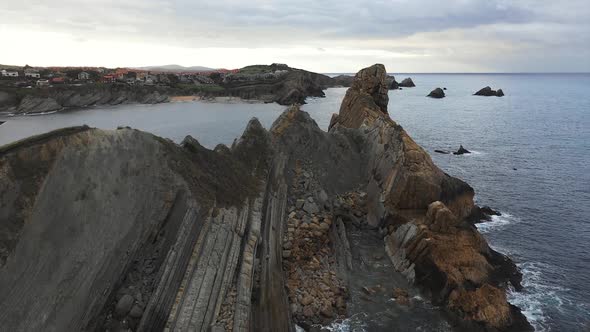 Stone peaks and seashore and foamy waves under cloudy sky