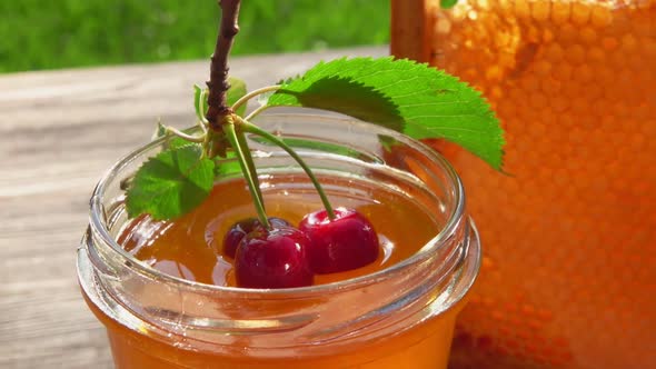 Two Large Cherries on the Twig with Leaves are Dipped Into Fresh Honey in a Jar