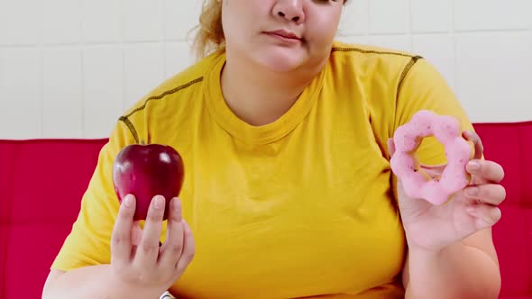 Overweight young woman choosing between donut and apple