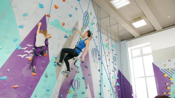 Kid and Young Lady Climbing Indoors in Sports Center Being Supported By Companions