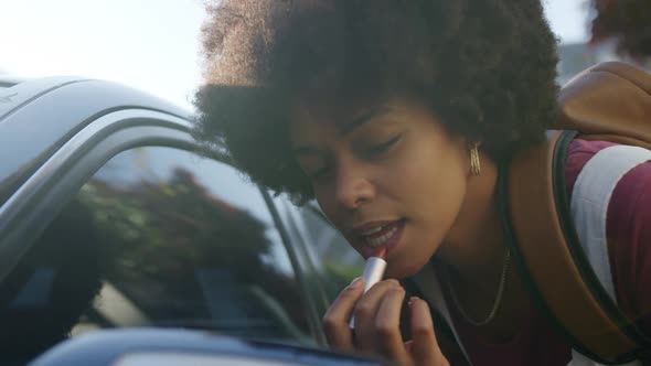 Mixed race woman putting lipstick in rear-view mirror