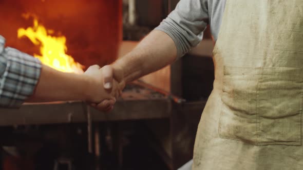Two Blacksmiths Shaking Hands and Bumping Fists at Work