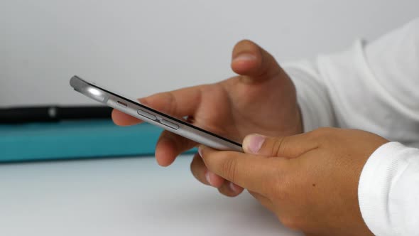 A child girl holds a phone in her hands, sits at the table, and does her homework.