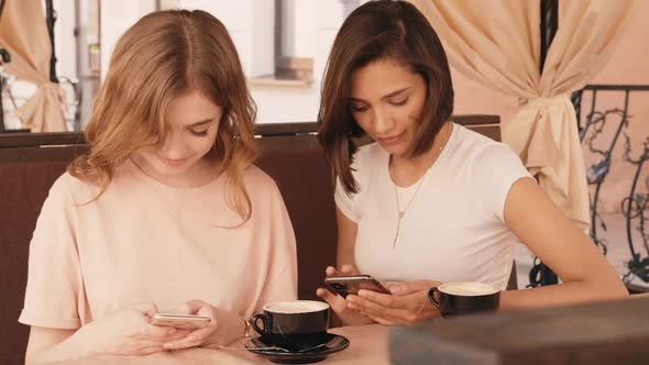 Two young beautiful smiling hipster girls chatting in cafe