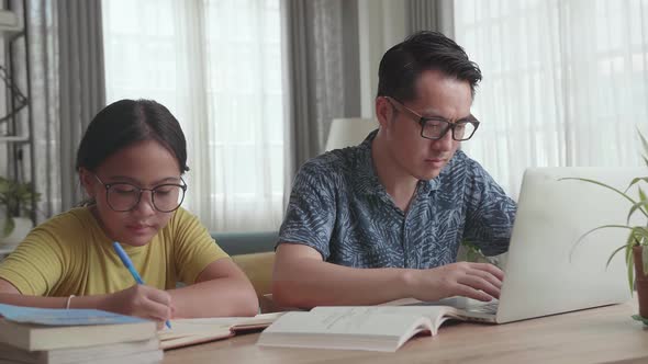 Father Working With Laptop And Daughter Doing Homework At Living Room