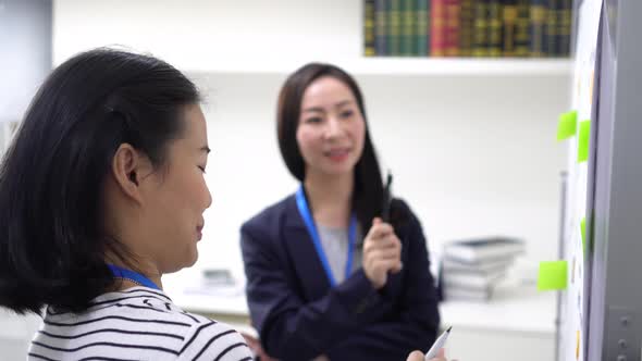 Young Asian Woman Writing Ideas on White Board While Middle Age Woman is Watching Indoors