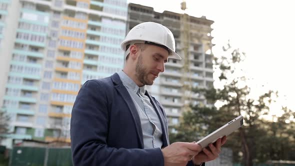 Construction engineer in a white helmet amends construction plans on a tablet