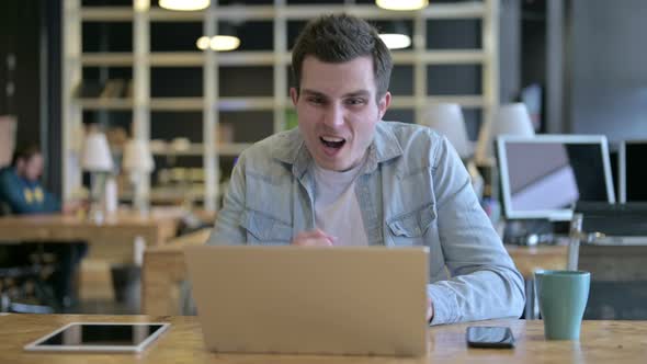 Surprised Young Designer Celebrating Success on Laptop in Office