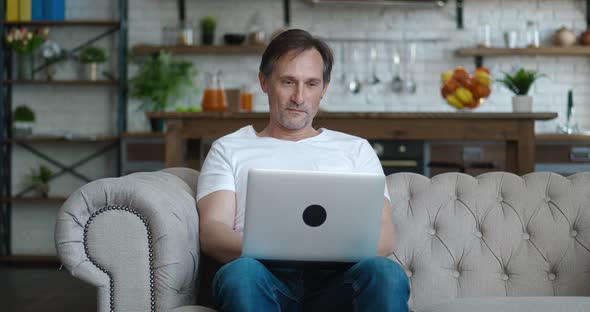 Mature Man Using Laptop Device on Sofa at Home Office Portrait of Male Working Distantly on Computer