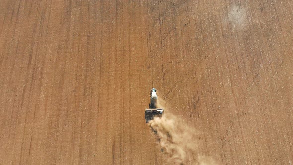 Top View Tractor with Harrow System Plowing Ground on Cultivated Farm Field Pillar of Dust Trails