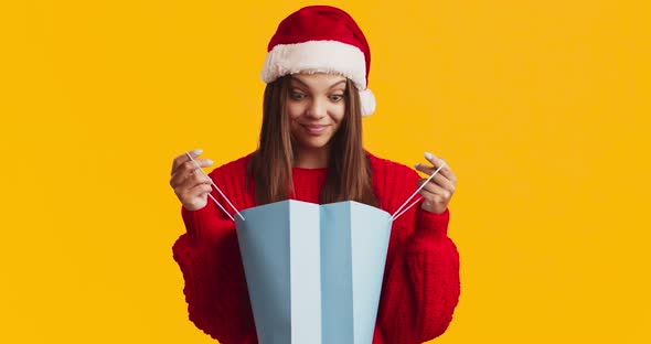 Surprised Young Woman in Santa Hat Looking Inside of Shopping Bag, Found Perfect Christmas Gift