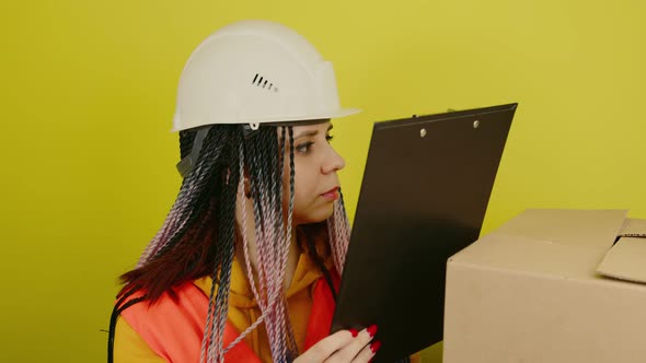 Female Construction Worker in Overalls with Clipboard and Big Box