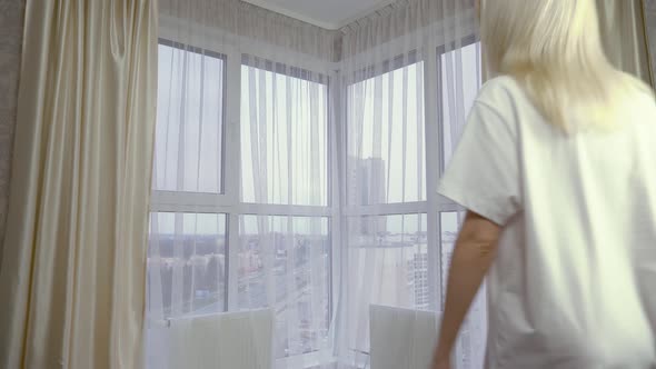 a woman opens the curtains in a room and looks out the windows in her underwear