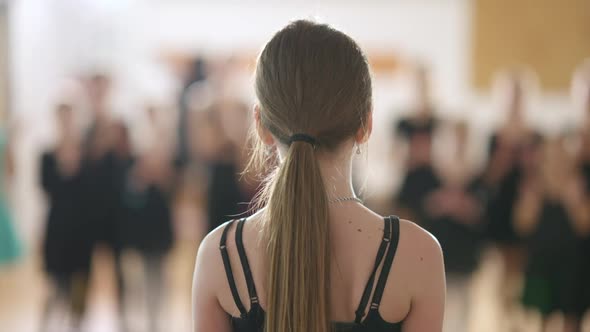 Back View Closeup of Caucasian Girl Standing in Dancing School with Blurred Children Clapping at