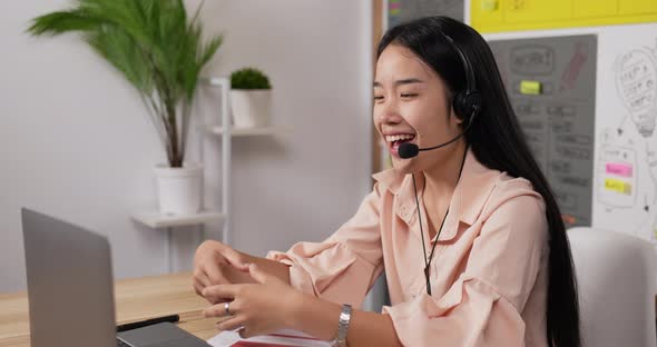 Asian woman with headset using laptop and talking