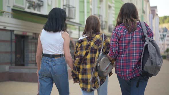 Back View Happy Girlfriends Strolling on City Street Holding Hands Talking