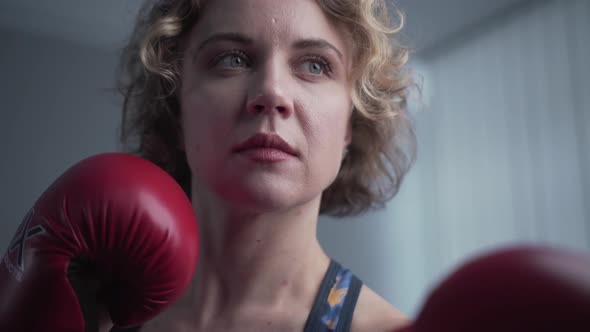 Young Beautiful Slim Woman Posing in Red Boxing Gloves in the Gym Against the Background of a Gray