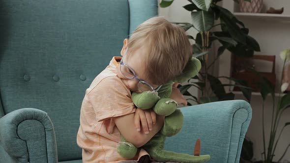 Happy Child in Eyeglasses Hugs Soft Dinosaur Toy Strokes Regrets and Kisses at Home