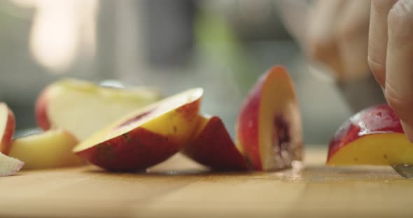 Young guy cutting a peach on wooden table in kitchen for prepare a fruit milkshake