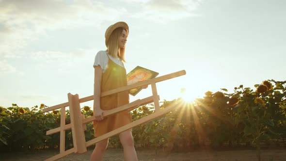 A Young Woman is Carrying an Easel and a Painting