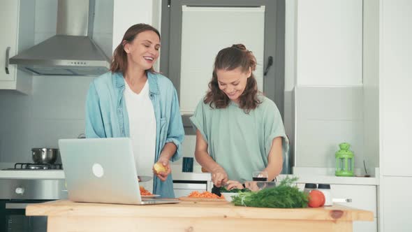 Two Young Women Dancing While Cooking and Talking with Friends Via the Internet