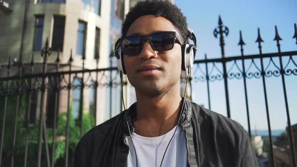 Portrait of Young Stylish Hipster Black Man in White Headphones and Sun Glasses Walking and Dancing