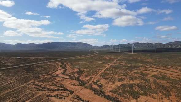 Drone aerial moving towards a wind farm in country Australia with mountains in the background and a