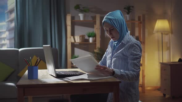 Worried Young Muslim Woman Sits in the Living Room at a Laptop and Counts Finances Money Problem