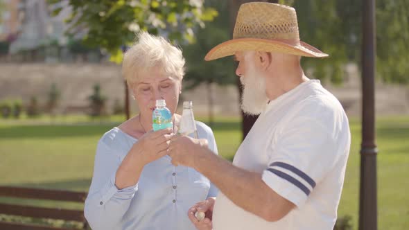 Middle-aged Caucasian Couple Drinking Tasty Water in the Summer Park and Chatting