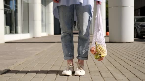 Unrecognizable woman walking with eco bag filled with fruits. Eco friendly, reusable shopping bag