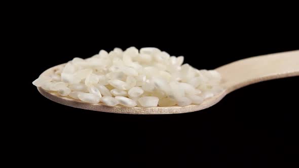 Full wooden spoon of uncooked white rice on a black background. 