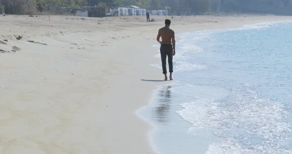 The Handsome Man with a Perfect Athletic Body in Gray Trousers Having Fun on a Deserted Beach in the