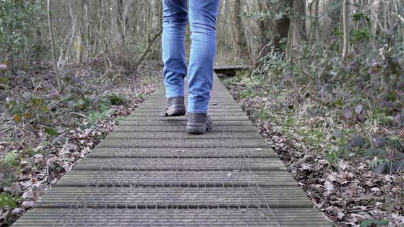 Unknown man walking in jeans on a wooden path in a forest. Slow-motion footage of 2 legs walking, fi