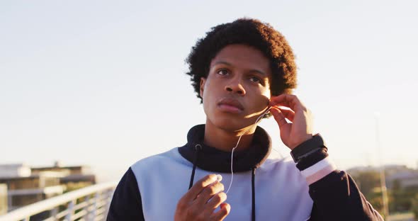 African american man putting earphones on during exercise outdoors