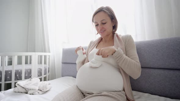 Young Pregnant Woman with Small Baby Shoes Sitting on Sofa at Home