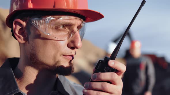 Closeup Face Male Engineer in Glasses and Helmet Talking Using Walkie Talkie at Construction Site