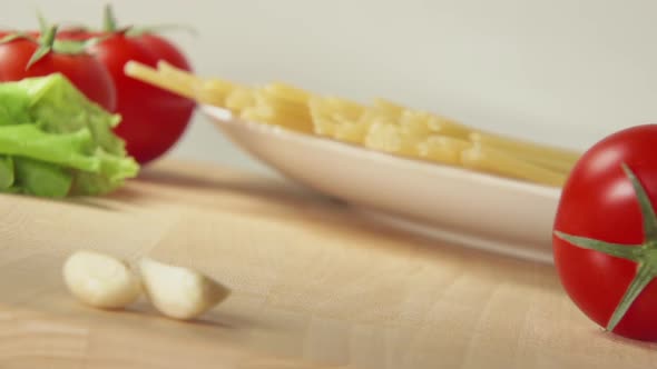 Ripe Tomato Rolls On A Table Near Spaghetti And Garlic