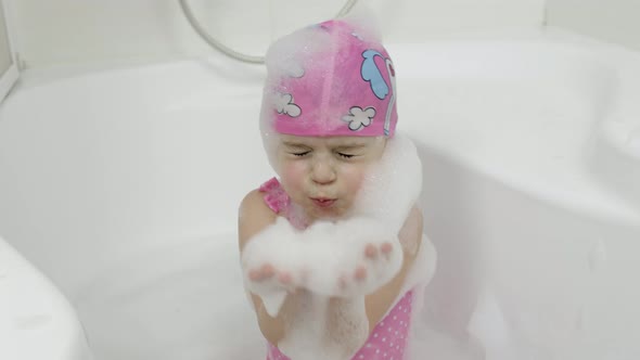 Cute Blonde Girl Takes a Bath in Swimwear. Little Child Washes Her Head