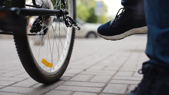 Closeup Legs of Unrecognizable Cyclist Male Putting Bike on Footrest on City Street Blurred