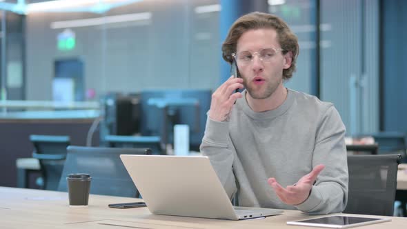 Angry Businessman with Laptop Talking on Smartphone