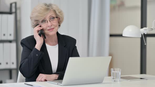 Old Businesswoman Talking on Phone While Working on Laptop