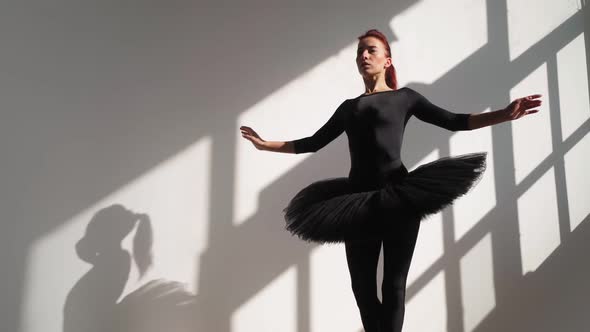 Ballerina in Black Tutu Gracefully Dances Against White Wall in Bright Sunlight